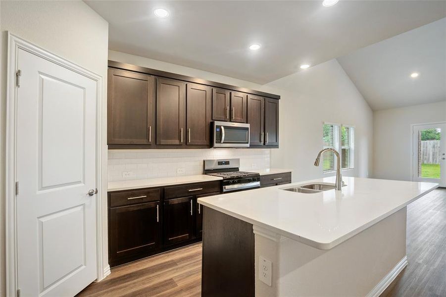 Kitchen featuring decorative backsplash, stainless steel appliances and an island with sink