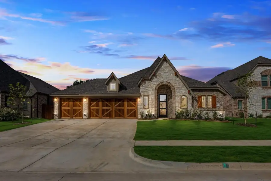 Single-story stone home with arched entry, wood garage doors, and manicured lawn at dusk