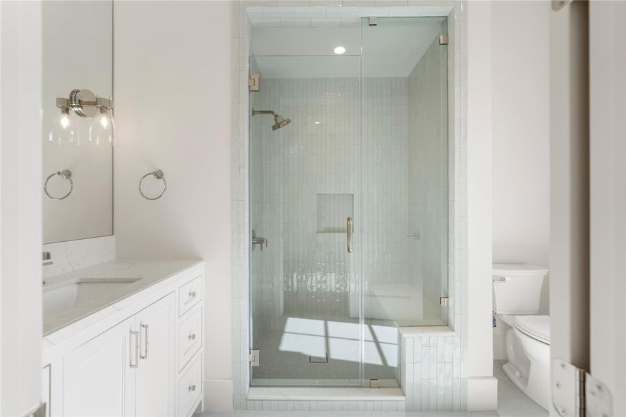 This secondary bathroom boasts porcelain flooring, an expansive walk-in shower, and plenty of storage. The shower is lined with quartzite and ceramic accents and houses polished nickel fixtures. The toilet is thoughtfully separated from the rest of the space. Note the cute soap shelf!
