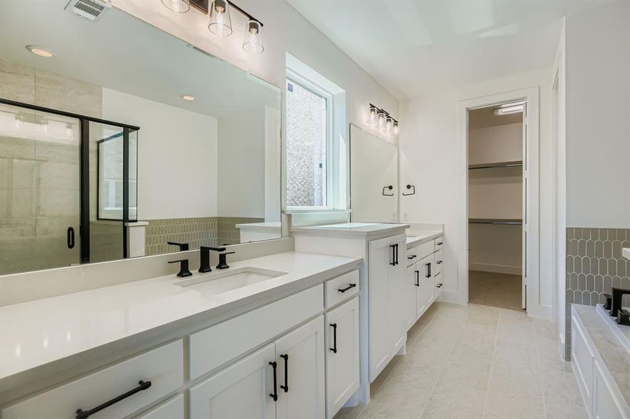 Full bathroom with a shower stall, two vanities, a spacious closet, light tile patterned floors, and tile walls