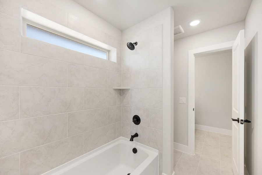 Bathroom with tub-shower combo, large tile surround, black fixtures, and a narrow window above the tub Bathroom with tub-shower combo, large tile surround, black fixtures, and a narrow window above the tub