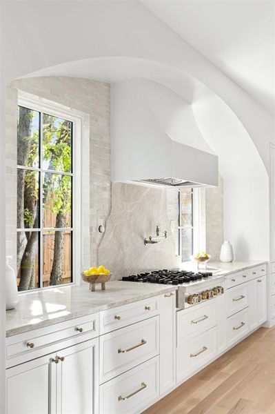 Kitchen featuring white cabinets, light stone countertops, decorative backsplash, and light wood-style floors Kitchen featuring white cabinets, light stone countertops, decorative backsplash, and light wood-style floors
