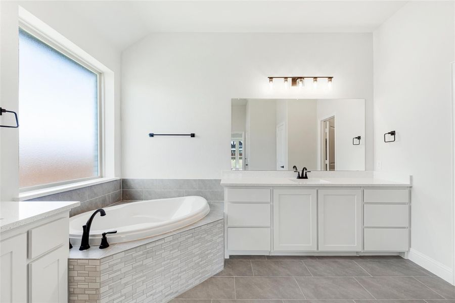 Master bathroom with soaking tub, tile surround, white vanity cabinets, and large mirror with overhead lighting.