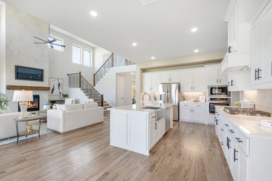 Open-concept kitchen with white cabinets and island flowing into living room with fireplace and staircase