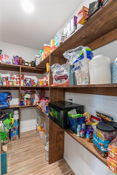 Walk-in pantry featuring extensive wood shelving, white walls, wood-finish flooring, and recessed ceiling lighting Walk-in pantry featuring extensive wood shelving, white walls, wood-finish flooring, and recessed ceiling lighting