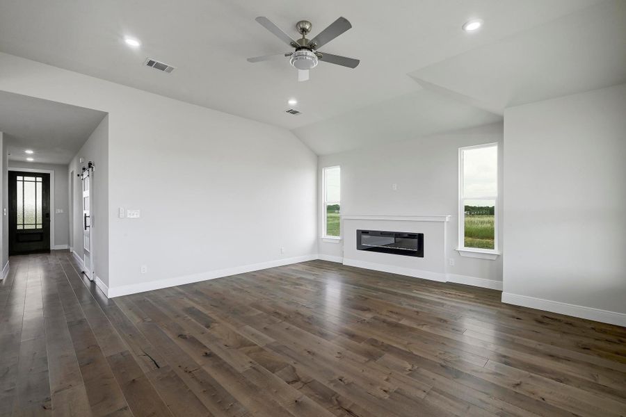 Unfurnished living room featuring dark wood-style flooring, a glass covered fireplace, a ceiling fan, lofted ceiling, and recessed lighting Unfurnished living room featuring dark wood-style flooring, a glass covered fireplace, a ceiling fan, lofted ceiling, and recessed lighting