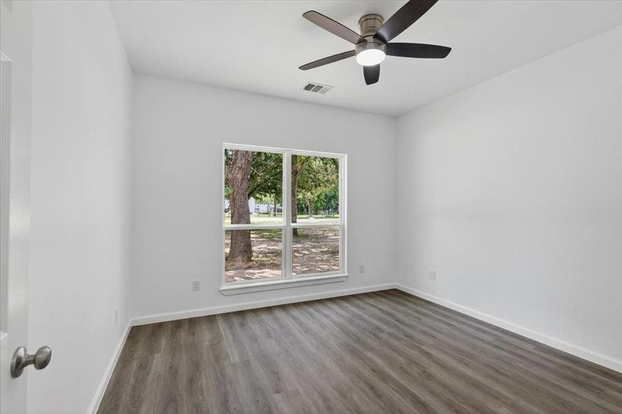 Bedroom 3 with view to front featuring LVP flooring, crisp white walls, a dual-pane window, and a ceiling fan with integrated lighting.