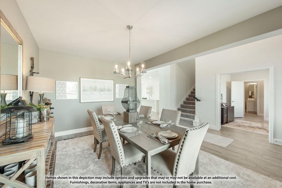 Dining room with gray table, upholstered chairs, chandelier, and hardwood floors open to staircase