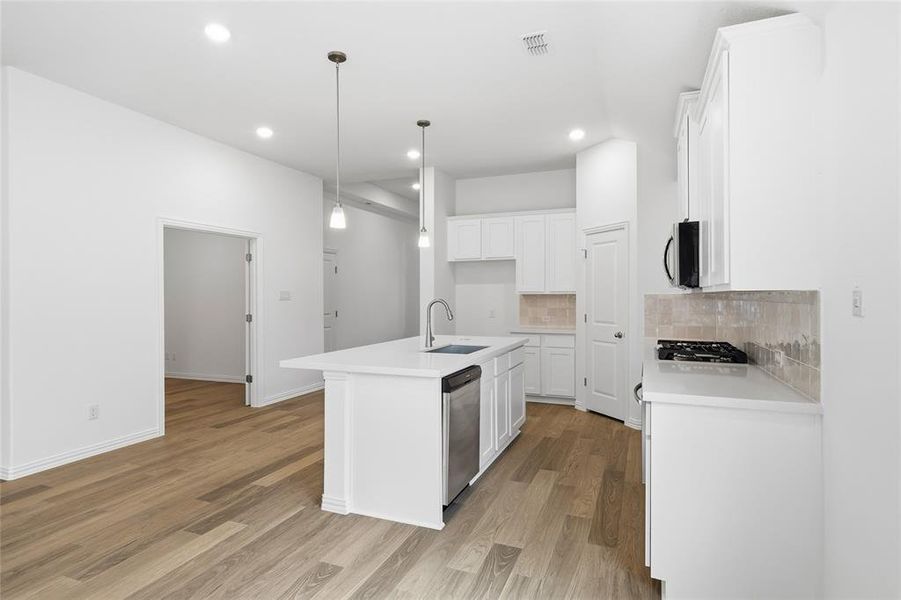 Modern kitchen featuring a white island with a stainless steel sink, pendant lighting, quartz countertops, and a tile backsplash