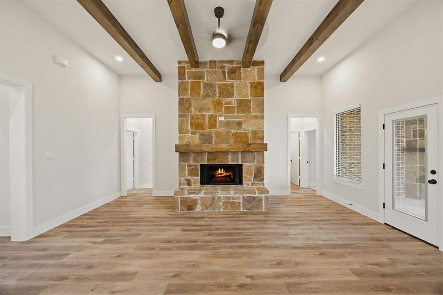 Spacious room featuring a stone-clad fireplace with a wood mantel, wood-finish flooring, exposed ceiling beams, recessed lighting, and a ceiling fan