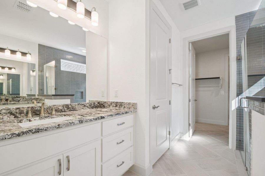 Full bath with vanity, a shower stall, a walk in closet, and light tile patterned floors Full bath with vanity, a shower stall, a walk in closet, and light tile patterned floors