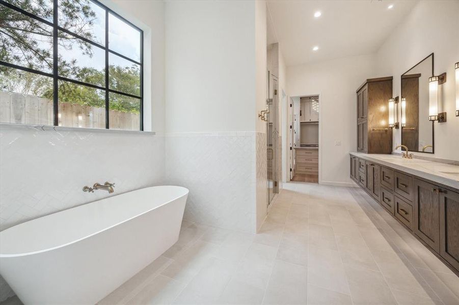 The spa-like primary bath includes a free-standing soaking tub, glass-enclosed shower, and a double vanity with rich wood cabinetry, offering a luxurious experience.