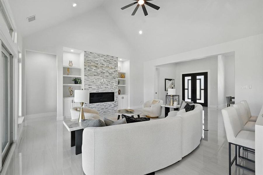 Living room featuring built in shelves, ceiling fan, high vaulted ceiling, a fireplace, and french doors Living room featuring built in shelves, ceiling fan, high vaulted ceiling, a fireplace, and french doors