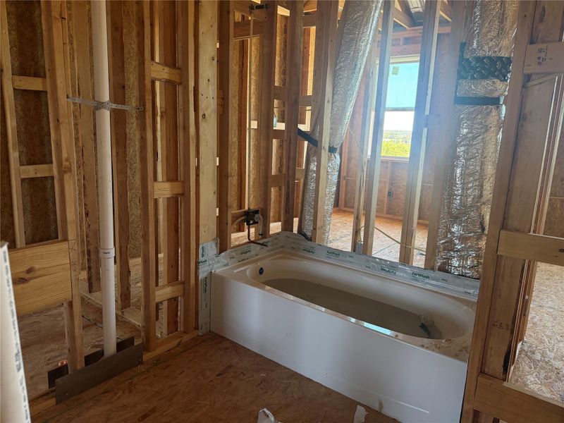 Exposed wood framing highlights the active bathroom construction phase surrounding a newly set tub.