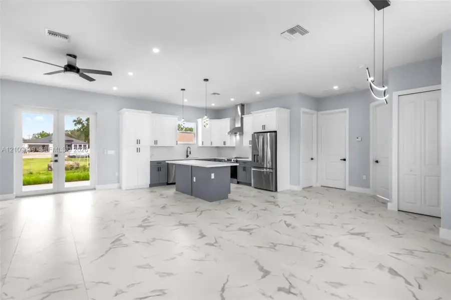 Open-concept kitchen featuring two-toned cabinetry, a central island with a stone-finish countertop, stainless steel appliances, porcelain tile flooring, and glass-paneled double doors