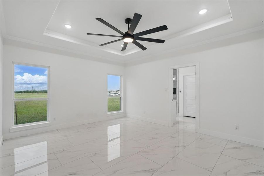 Empty room with a raised ceiling, baseboards, recessed lighting, ceiling fan, and light marble finish flooring Empty room with a raised ceiling, baseboards, recessed lighting, ceiling fan, and light marble finish flooring