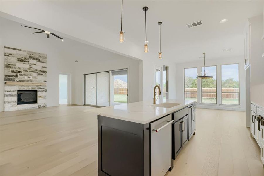 Dual tone kitchen with a tile fireplace, light wood-style flooring, open floor plan, a center island with sink, and dishwasher