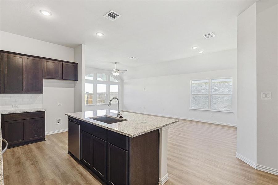 Kitchen featuring sink, light stone counters, light hardwood / wood-style flooring, stainless steel dishwasher, and backsplash