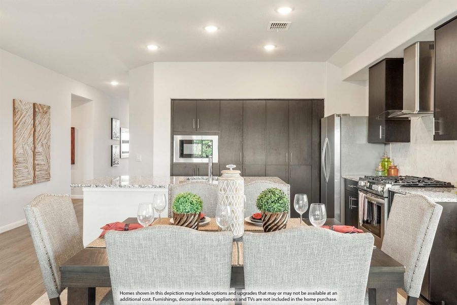 Open dining area with set table flows into kitchen with dark cabinets and stainless steel appliances Open dining area with set table flows into kitchen with dark cabinets and stainless steel appliances