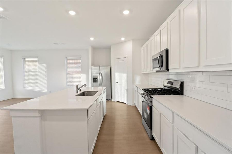 Kitchen with stainless steel appliances, white cabinets, light wood-style flooring, recessed lighting, and a kitchen island with sink