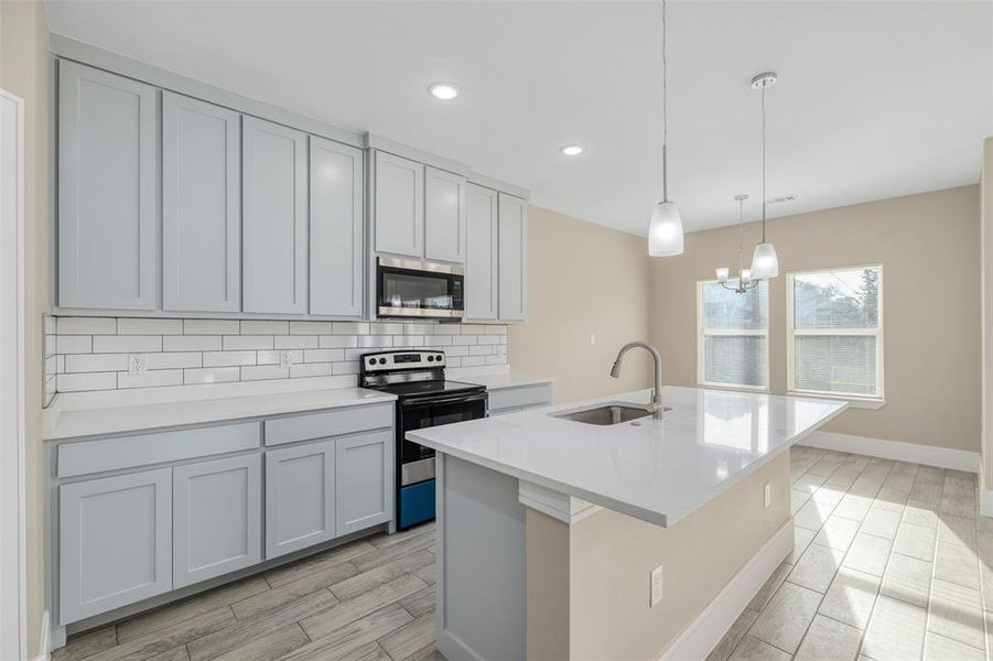 Kitchen featuring hanging light fixtures, sink, stainless steel appliances, and light wood-type flooring