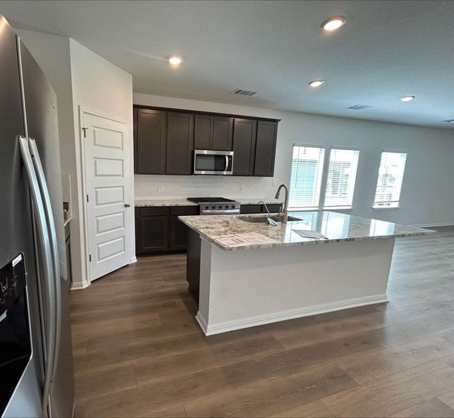 Kitchen featuring light stone counters, appliances with stainless steel finishes, tasteful backsplash, recessed lighting, and a center island with sink