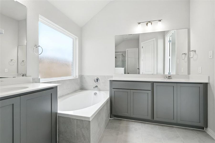 Bathroom with two vanities, a bath, a shower stall, lofted ceiling, and light tile patterned floors
