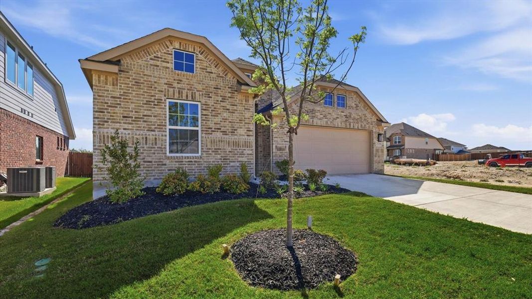 Brick exterior featuring a two-car garage, concrete driveway, and landscaping with mature plantings