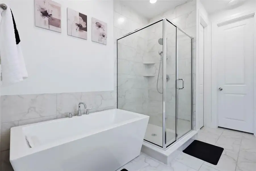Freestanding soaking tub with chrome fixtures, complemented by a glass-enclosed shower with tile surround
