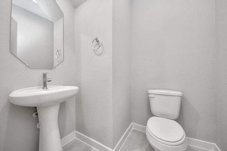 This half bathroom features a stylish pedestal sink, modern hardware, and bright recessed lighting, creating a sleek and inviting space. Sample photo of completed home with similar floor plan. Actual colors and selections may vary.