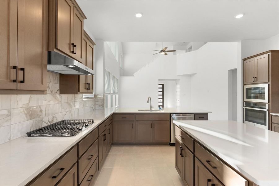 Kitchen featuring stainless steel appliances, under cabinet range hood, a sink, light countertops, and backsplash