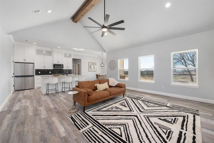 Living room with ceiling fan, high vaulted ceiling, light hardwood / wood-style floors, and beamed ceiling