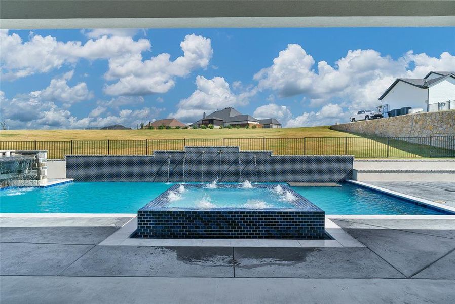 View of pool featuring pool water feature, a lawn, and a jacuzzi