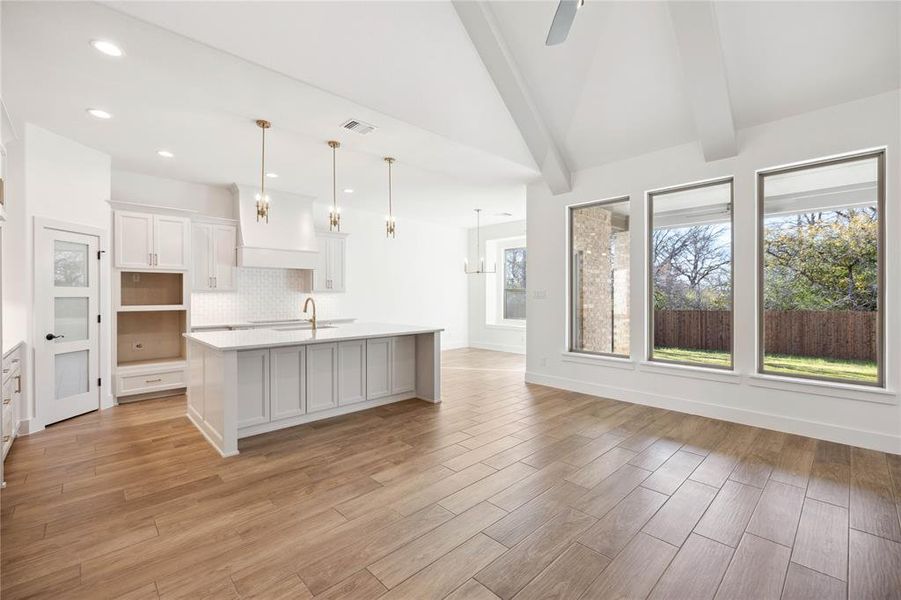 Kitchen featuring a kitchen island with sink, white cabinets, decorative light fixtures, and light wood-type flooring