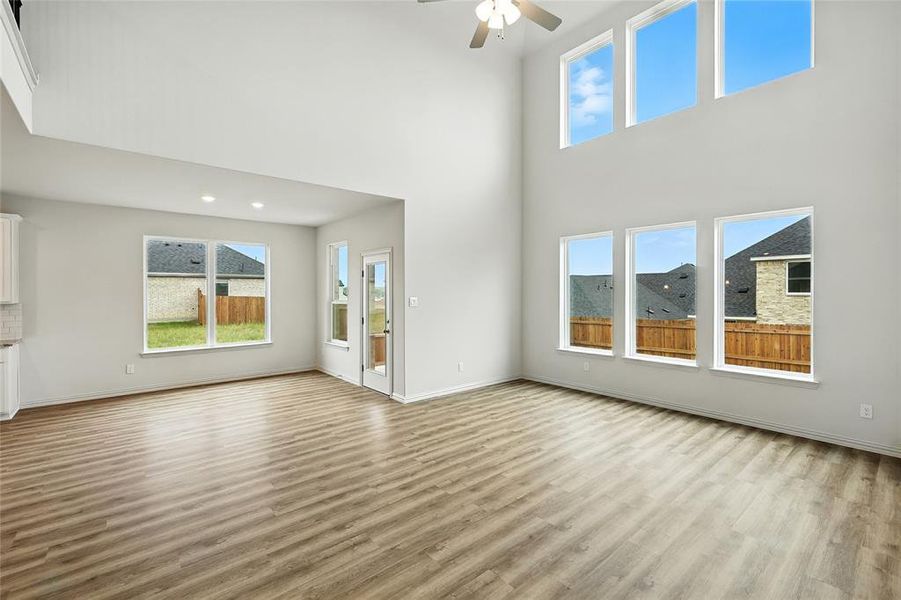Unfurnished living room featuring a ceiling fan, plenty of natural light, light wood-type flooring, and a high ceiling