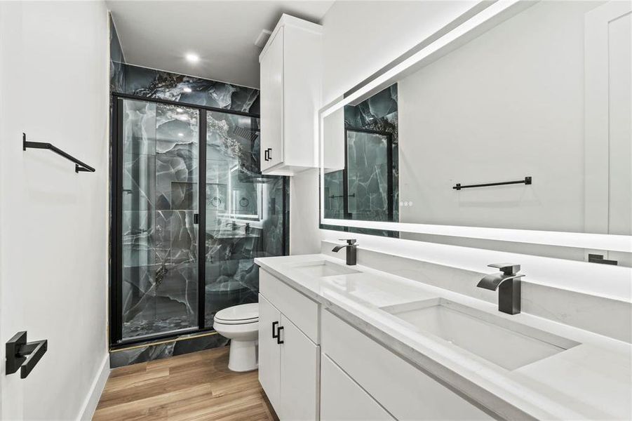 Full bath with double vanity, a marble finish shower, and light wood-style floors