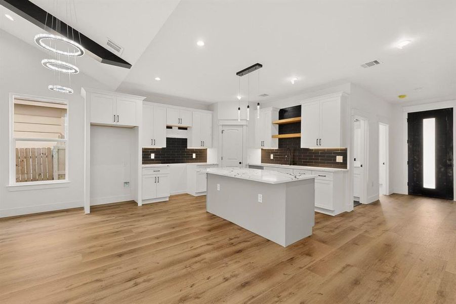 Kitchen with a kitchen island, white cabinetry, light wood-type flooring, hanging light fixtures, and lofted ceiling Kitchen with a kitchen island, white cabinetry, light wood-type flooring, hanging light fixtures, and lofted ceiling