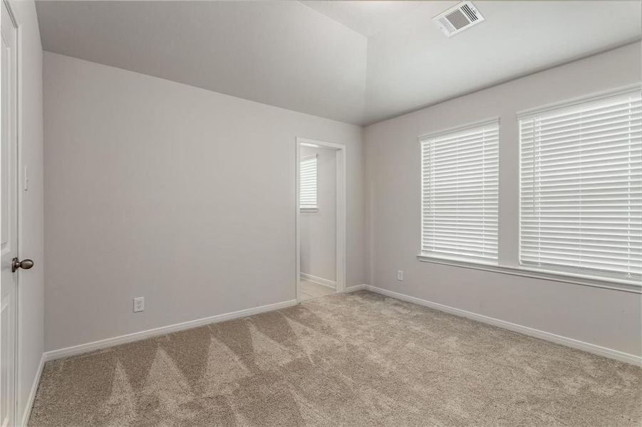 A spacious and serene bedroom, bathed in natural light from the large windows. The neutral color palette and plush carpeting create a cozy and inviting atmosphere. The adjoining bathroom promises convenience and privacy, making this space perfect for relaxation and comfort. Photos are from another Rylan floor plan.