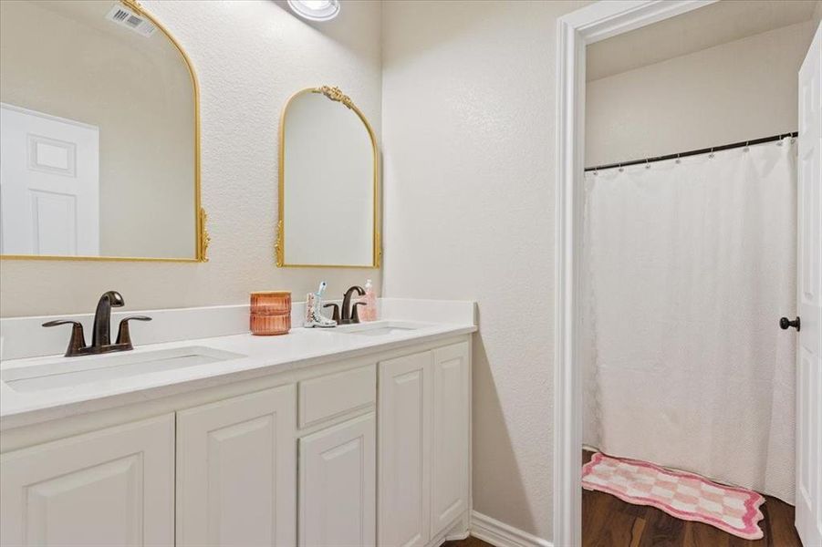 Bathroom featuring double vanity, dark wood finished floors, a textured wall, and a shower with curtain