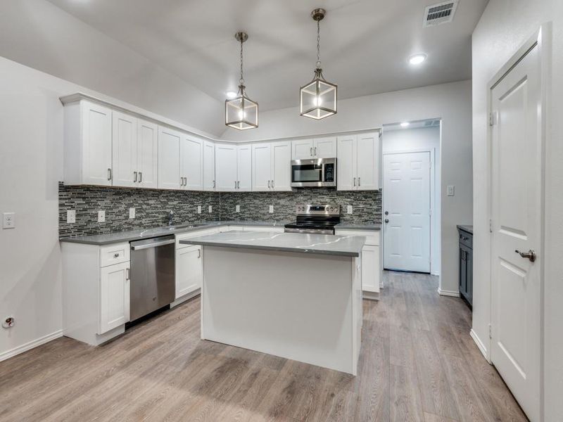 Kitchen featuring decorative backsplash, light hardwood / wood-style floors, a kitchen island, stainless steel appliances, and white cabinets