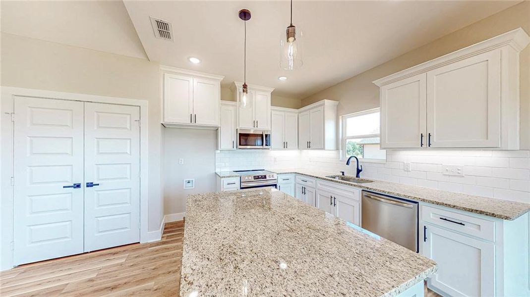 Kitchen with light stone counters, appliances with stainless steel finishes, light wood finished floors, a kitchen island, and backsplash Kitchen with light stone counters, appliances with stainless steel finishes, light wood finished floors, a kitchen island, and backsplash