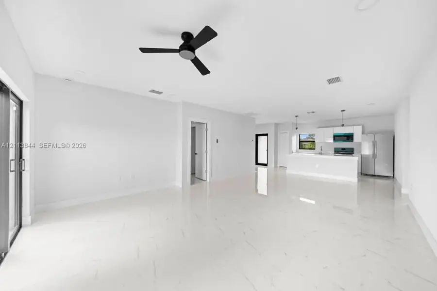 Open-concept interior featuring large-format stone-finish flooring, a matte black ceiling fan, recessed lighting, and kitchen cabinetry paired with stainless steel appliances Open-concept interior featuring large-format stone-finish flooring, a matte black ceiling fan, recessed lighting, and kitchen cabinetry paired with stainless steel appliances
