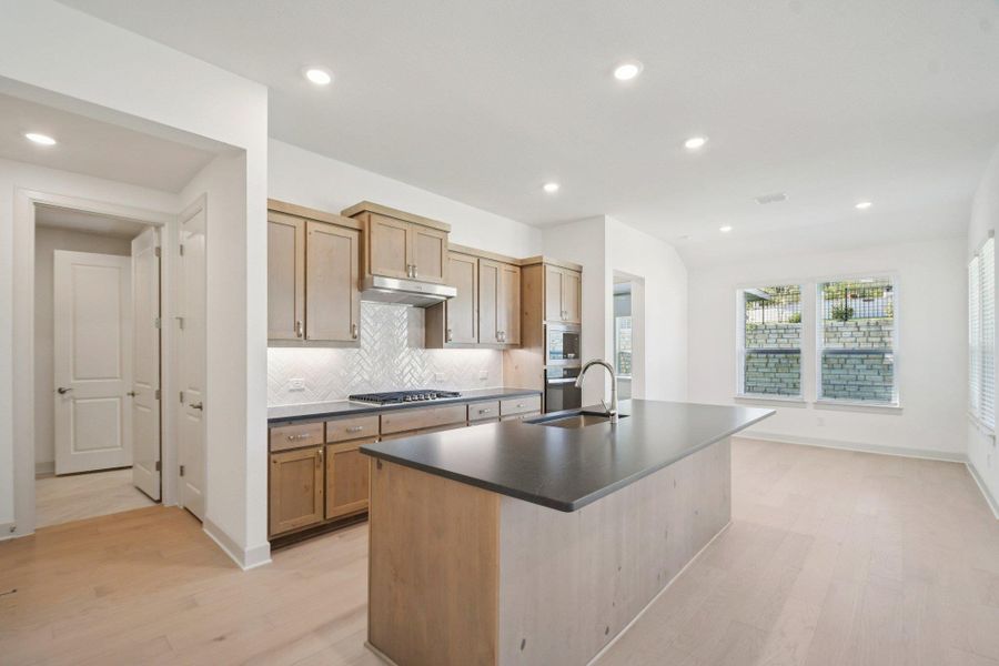 Kitchen featuring backsplash, recessed lighting, an island with sink, light wood-style flooring, and light brown cabinets Kitchen featuring backsplash, recessed lighting, an island with sink, light wood-style flooring, and light brown cabinets