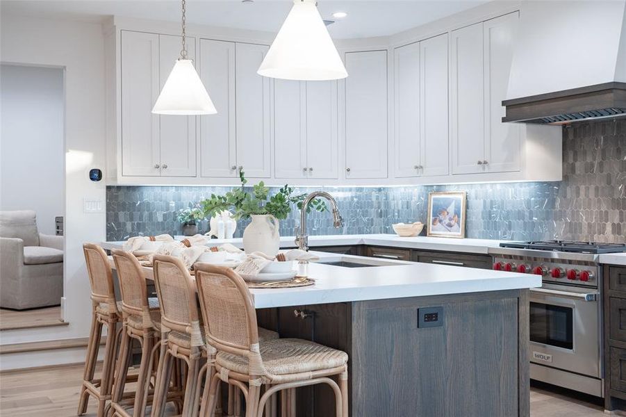 Kitchen with white cabinets, premium stove, light wood-type flooring, custom range hood, and pendant lighting