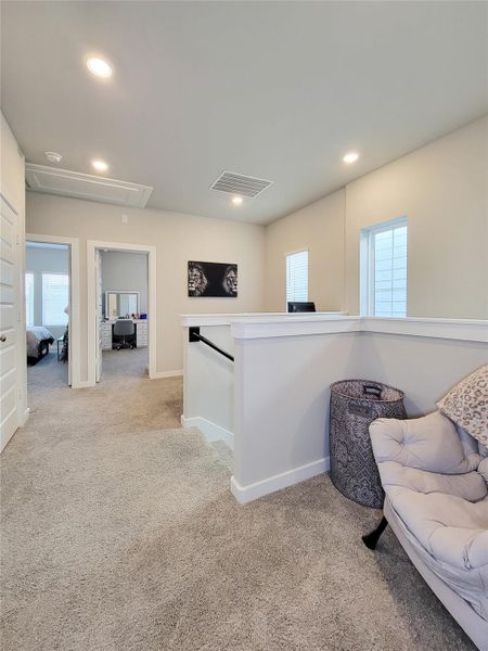 Showcases a bright, carpeted landing area with recessed lighting, featuring a cozy chair and decorative elements. It connects to a bedroom and home office space, offering a functional and inviting upstairs layout.