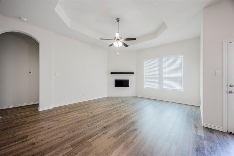 Unfurnished living room featuring ceiling fan, a tray ceiling, and dark wood-type flooring