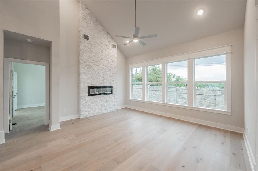 Unfurnished living room featuring high vaulted ceiling, ceiling fan, light wood-style flooring, and a stone fireplace