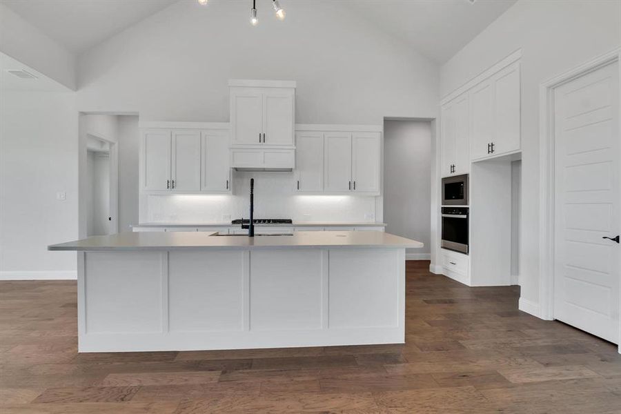 Kitchen featuring oven, dark wood-type flooring, white cabinets, and a kitchen island with sink