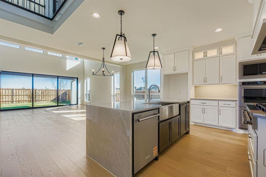 Kitchen featuring light wood finished floors, open floor plan, light stone counters, hanging light fixtures, and tasteful backsplash Kitchen featuring light wood finished floors, open floor plan, light stone counters, hanging light fixtures, and tasteful backsplash