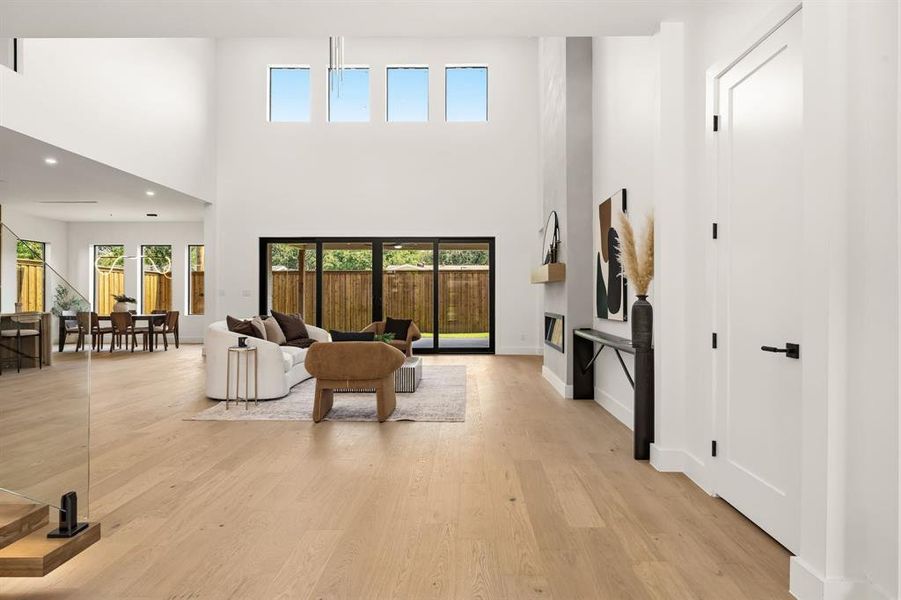Two-story living area featuring light wood-finish flooring, a contemporary fireplace, and a wall of glass sliding doors
